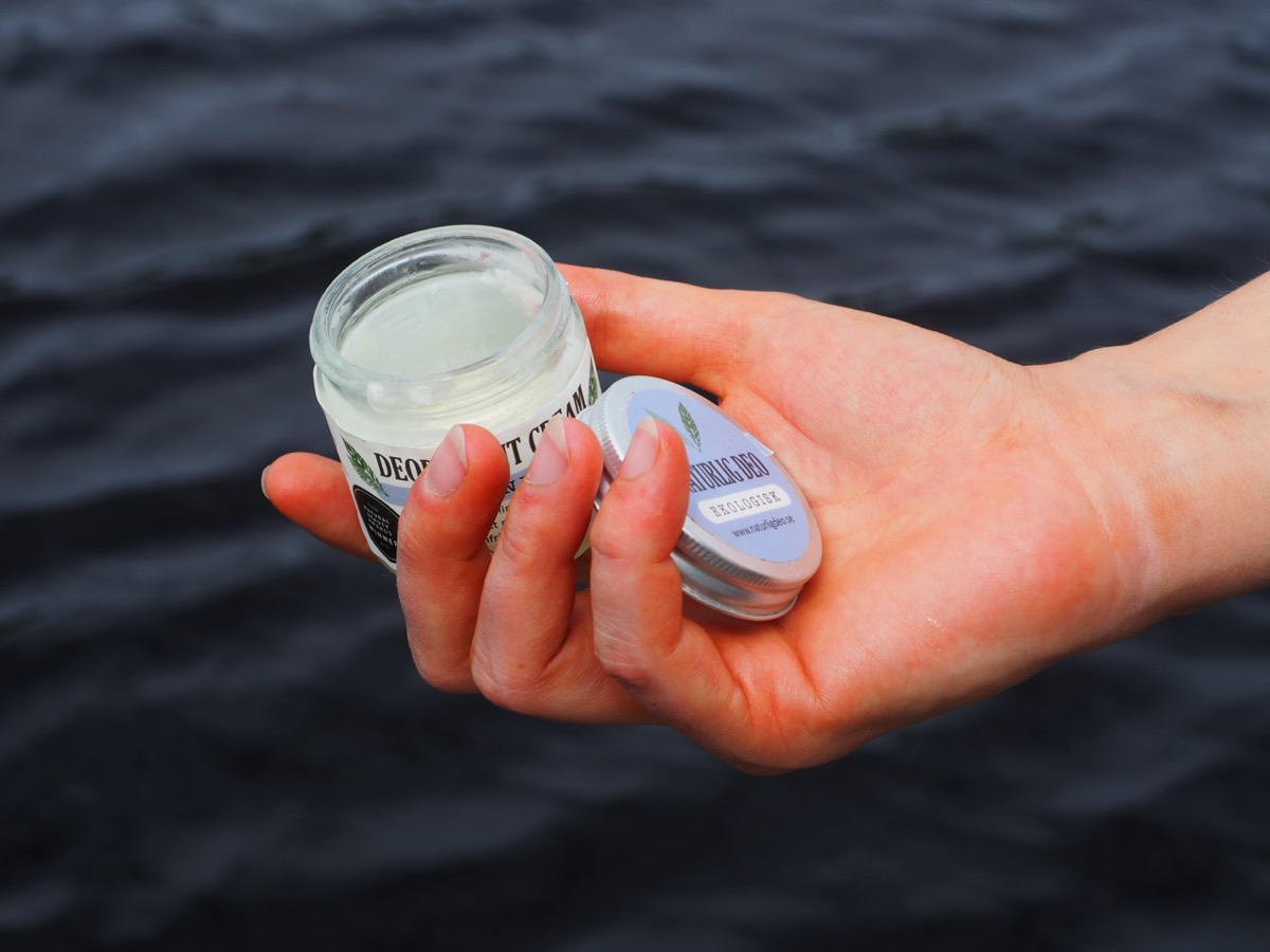 En öppnad burk deodorantkräm från Naturlig Deo i en hand vid vattnet